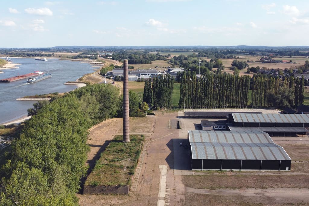 Dronebeeld van het terrein van de voormalige steenfabriek De Ooij met de schoorsteen, de loodsen en de Waal